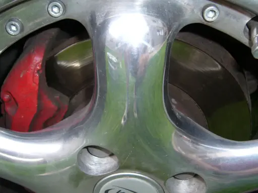 Błyszczące polerowanie aluminium felgi z widocznym czerwonym zaciskiem hamulcowym i tarczą.