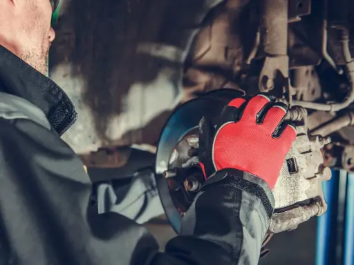 Mechanik w czerwonych rękawicach pracuje nad układem hamulcowym, przygotowując wymianę przewodów hamulcowych.