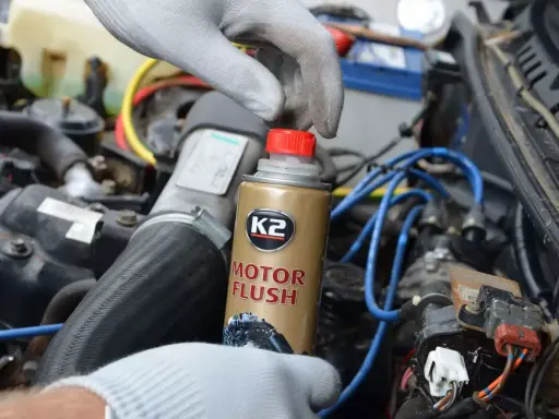 Ręka w rękawiczce trzyma puszkę K2 Motor Flush, najlepsza płukanka do silnika benzynowego, gotowa do użycia w samochodzie.