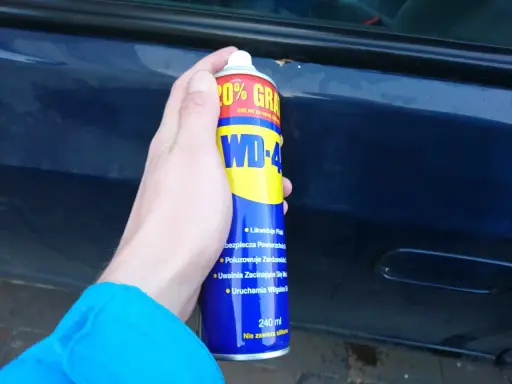 Dłoń trzyma puszkę WD-40, gotową do usuwania rdzy z samochodu.