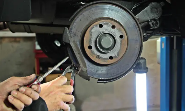 Mechanik wymienia klocki hamulcowe. Widać zużyte tarcze hamulcowe i narzędzia.