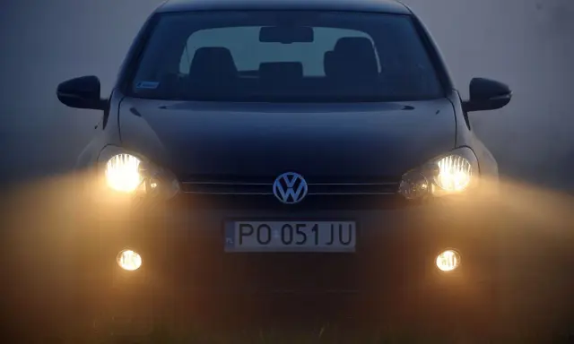 Ciemny Volkswagen z włączonymi światłami przeciwmgielnymi przednimi, poprawiającymi widoczność w mgle.