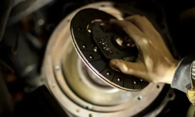 Dłoń trzymająca tarczę sprzęgła nad mechanizmem w samochodzie.
