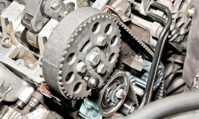 Zbliżenie na mechanizm rozrządu silnika, widoczny jest czujnik położenia wałka rozrządu, koło pasowe i pasek.