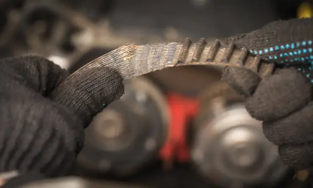 Zużyty pasek klinowy w rękach mechanika, przygotowanie do wymiany.