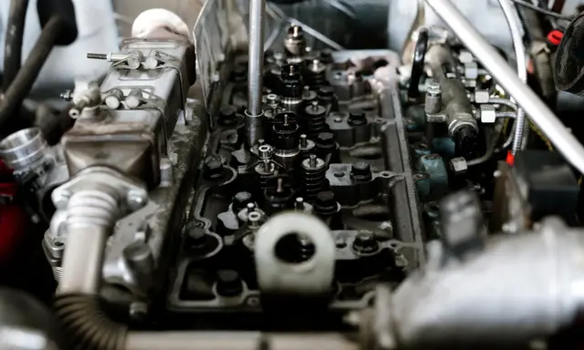 Widok wnętrza silnika z widocznymi zaworami i sprężynami. Widać fragmenty układu paliwowego i metalowe elementy, które są częścią mechanizmu, gdzie pracują tłoki.
