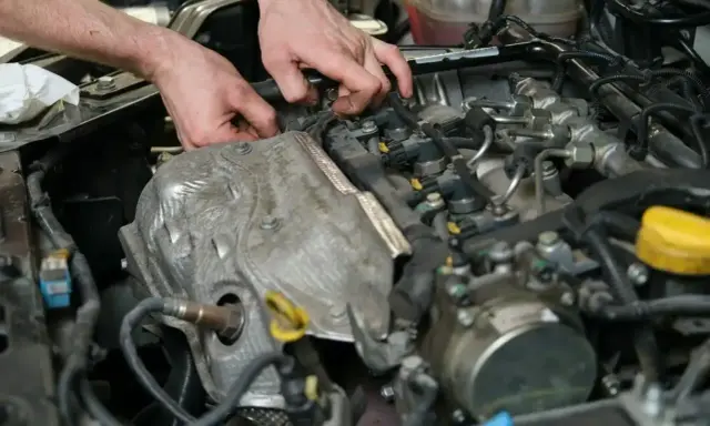 Ręce mechanika pracujące przy silniku samochodowym, widoczne elementy układu paliwowego i czujnik.