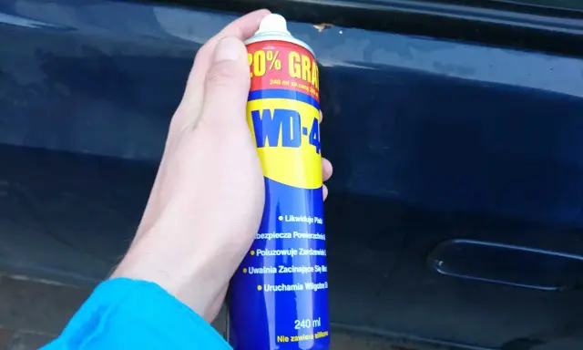 Dłoń trzyma puszkę WD-40, gotową do usuwania rdzy z samochodu.