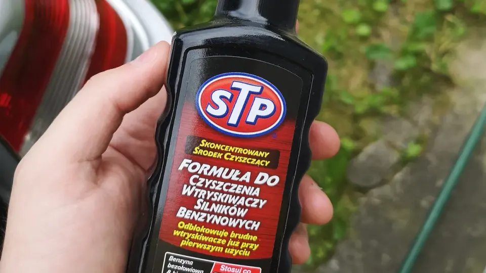 Dłoń trzyma butelkę STP z formułą do czyszczenia wtryskiwaczy silników benzynowych.