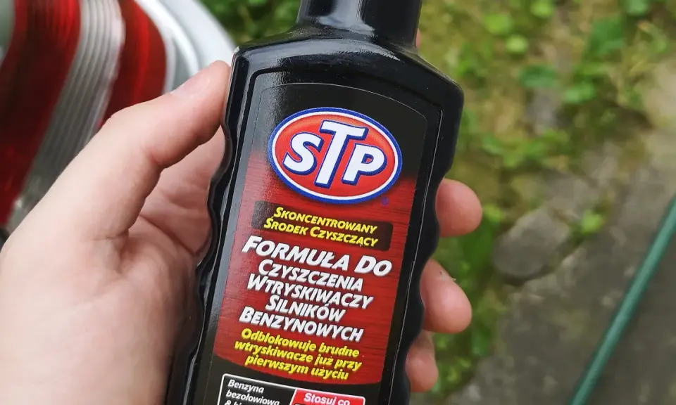 Dłoń trzyma butelkę STP z formułą do czyszczenia wtryskiwaczy silników benzynowych.