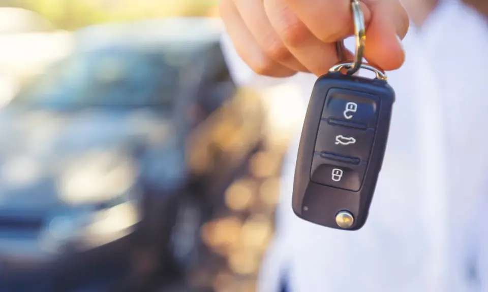 Dłoń trzyma kluczyk samochodowy z ikonami otwierania, bagażnika i zamykania. Kontrolka immobilizera na kluczyku jest gotowa do uruchomienia pojazdu.