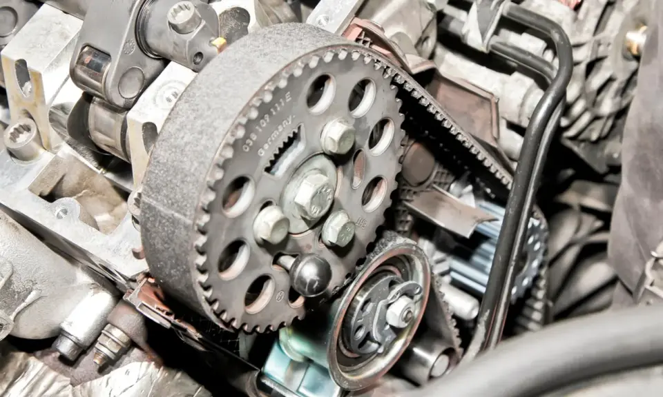 Zbliżenie na mechanizm rozrządu silnika, widoczny jest czujnik położenia wałka rozrządu, koło pasowe i pasek.
