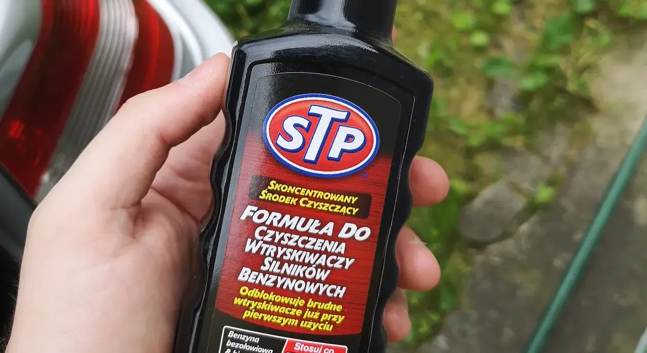 Dłoń trzyma butelkę STP z formułą do czyszczenia wtryskiwaczy silników benzynowych.