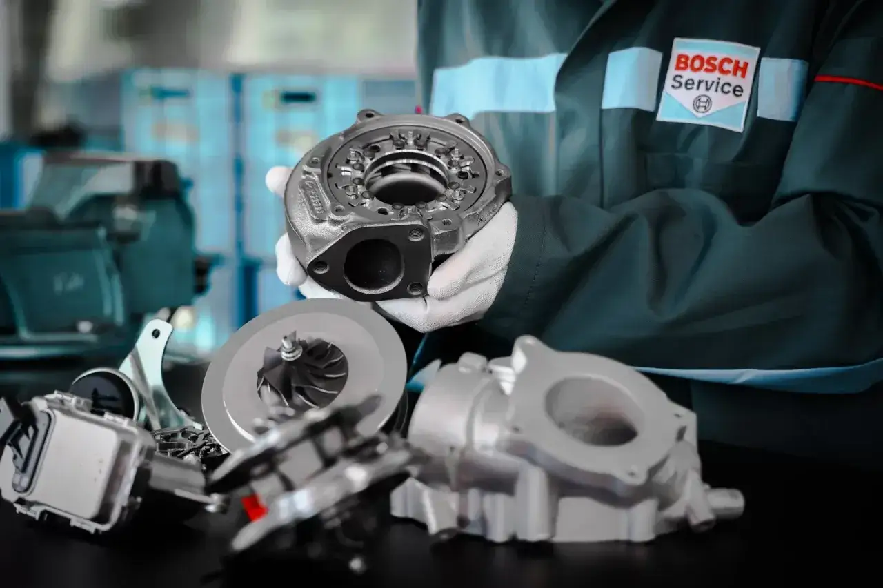 Mechanik w fartuchu Bosch Service prezentuje części turbosprężarki. Rozpoznaj uszkodzona turbina objawy i przyczyny awarii.