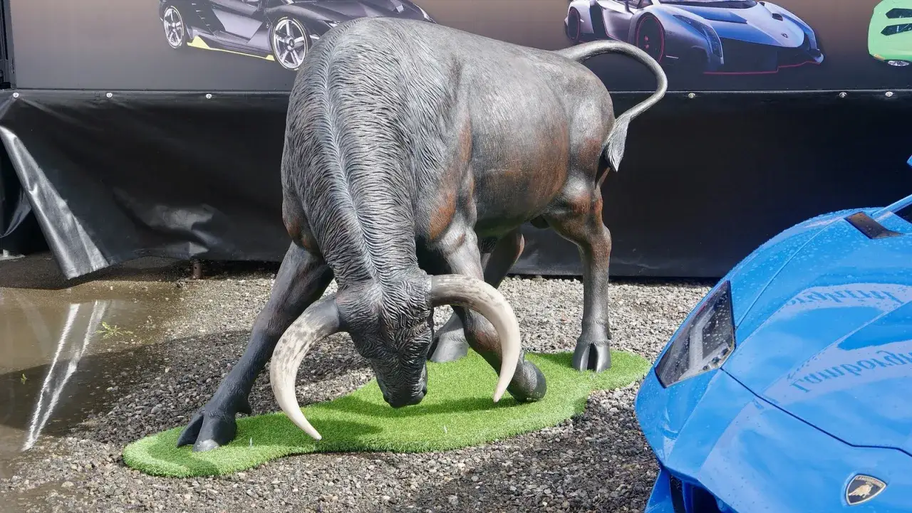 Byk, symbol marki, jak wygląda znaczek Lamborghini. Obok niebieski supersamochód.
