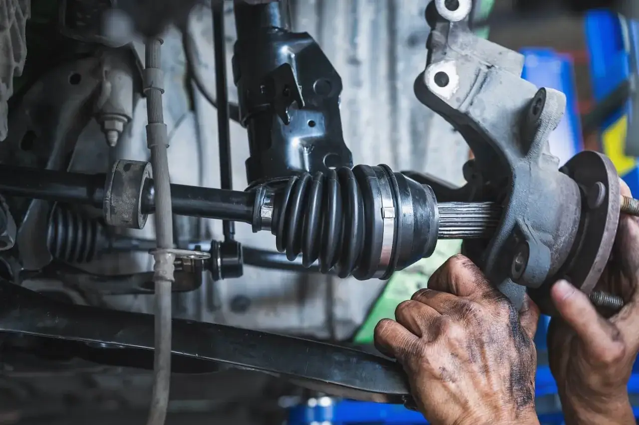 Mechanik wymienia zużyte półosie w samochodzie. Widać gumową osłonę przegubu i zębatą końcówkę półosi.