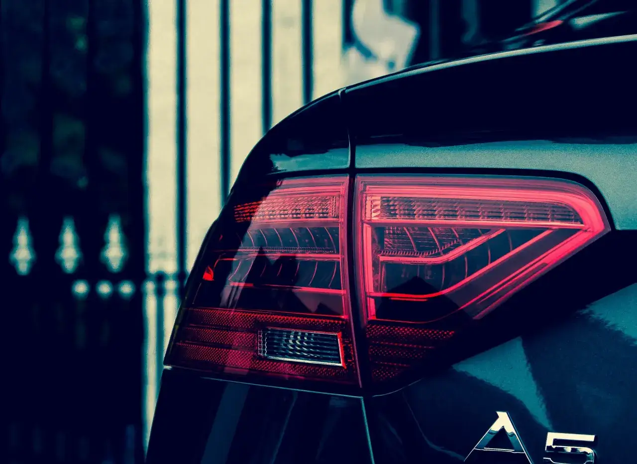 Czerwone światło tylnej lampy samochodu Audi A5, z widocznym napisem A5. Polimocznikowa obudowa lampy lśni w ciemności.