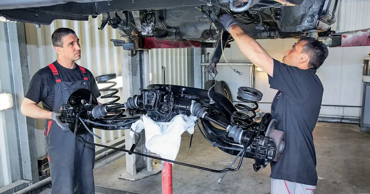 Mechanicy pracują nad wymianą przewodów hamulcowych w podniesionym samochodzie.