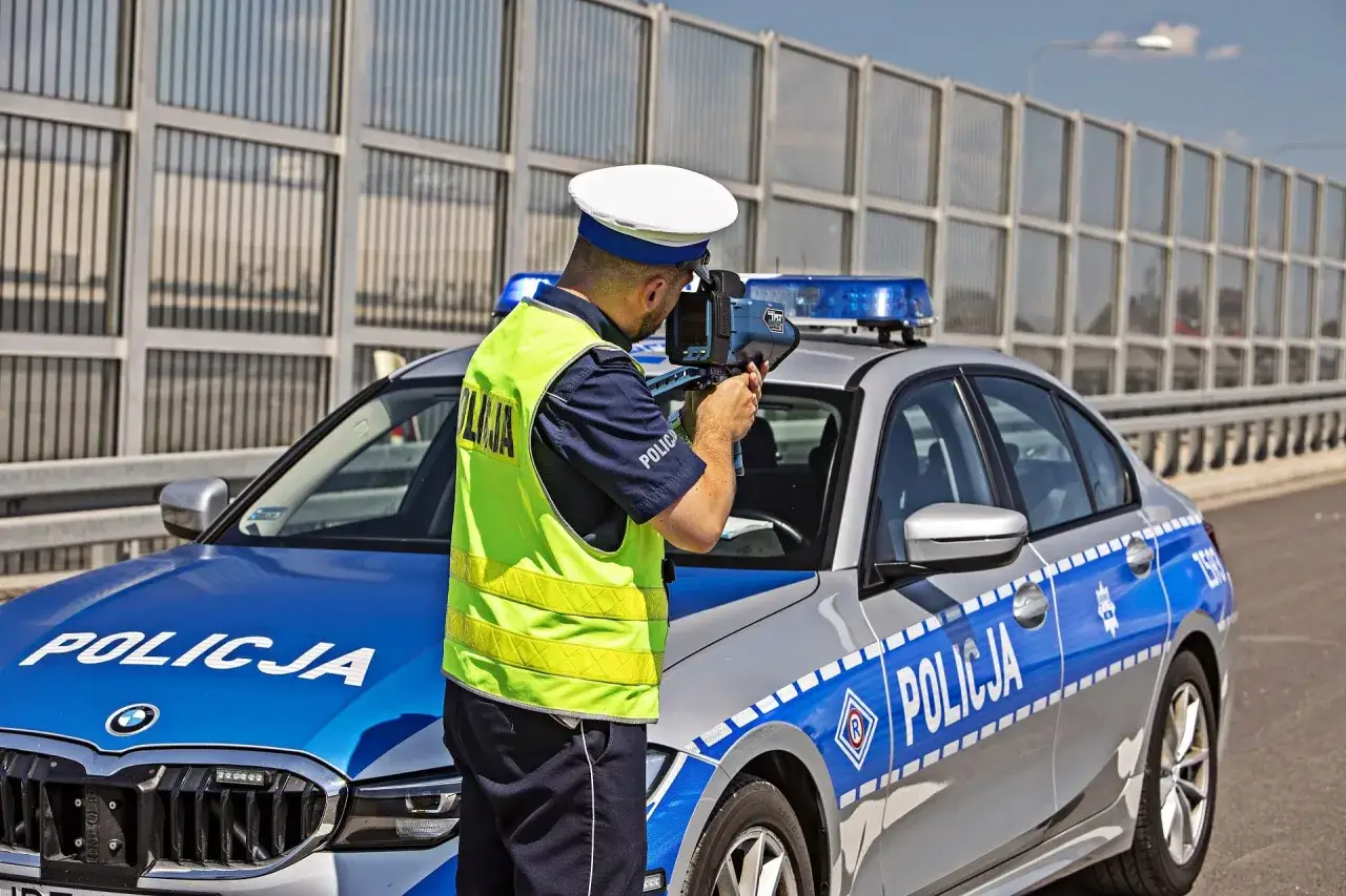 Policjant mierzy prędkość radiowozem, gotowy wystawić mandat za przekroczenie prędkości.