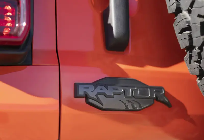 Pomarańczowy lakier lśni, a czarne, wyraziste logo "RAPTOR" z pazurami podkreśla jego dziką naturę.